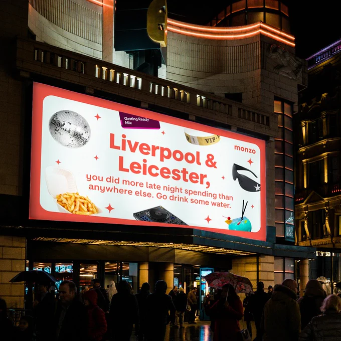 An illuminated billboard at night, with the text reading 'Liverpool & Leicester, you did more late night spending than anywhere else. Go drink some water.' The text is surrounded by a disco ball, chips and sunglasses