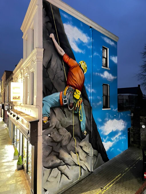 Street art on a gable wall in Ballymena town centre showing a climber scaling a cliff face with blue sky behind