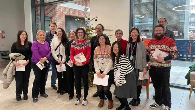 13 people standing in front of a Christmas tree, with copies of 100 Carols for Choirs