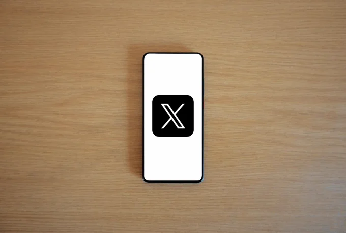 A smartphone with the screen displaying a large black 'X' on a white background, placed on a wooden surface.