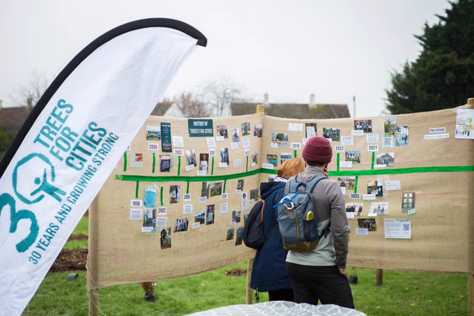 People looking at a visual timeline of Trees for Cities history at a planting event (with a branded flag on the left)