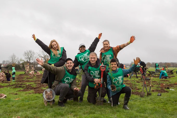 A group of Trees for Cities volunteers (and a dog) pose with their arms in their air at a planting event