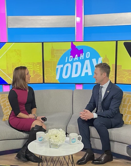 U.S. Attorney Josh Hurwit and KTVB's Melissa Paul sit down for an interview on Idaho Today. The screen behind them shows Idaho and reads: IDAHO TODAY. Mugs and flowers appear on the table between them.