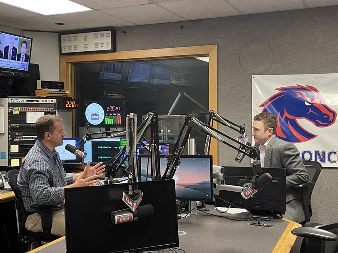 U.S. Attorney Hurwit and KBOI NewsTalk Radio Host Nate Shelman in the studio talking into mics. Many screens and mics appear on the desk between them. A BSU Bronco sign appears behind Josh.