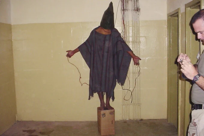 Abdou Hussain Saad Faleh pictured standing on a box with wires attached to his left and right hand.
Abdou was told by U.S. Army prison guards that he would be electrocuted if he fell off the box.
Abu Ghraib prison, Iraq 4 November 2003