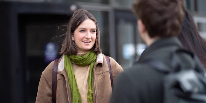 Two people engaging in a conversation outdoors, with one person facing the camera smiling.
