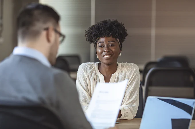 A young black woman is smiling in her interview, she's being interviewed by a white man in glasses. 
