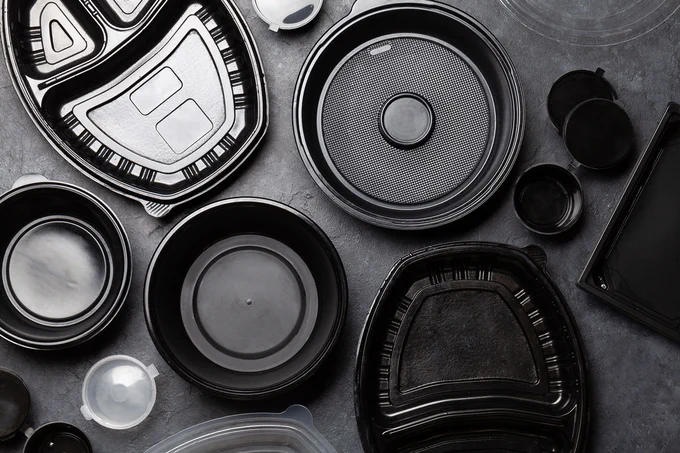 Various clean black plastic containers for carryout or delivery food spread neatly across a gray surface.