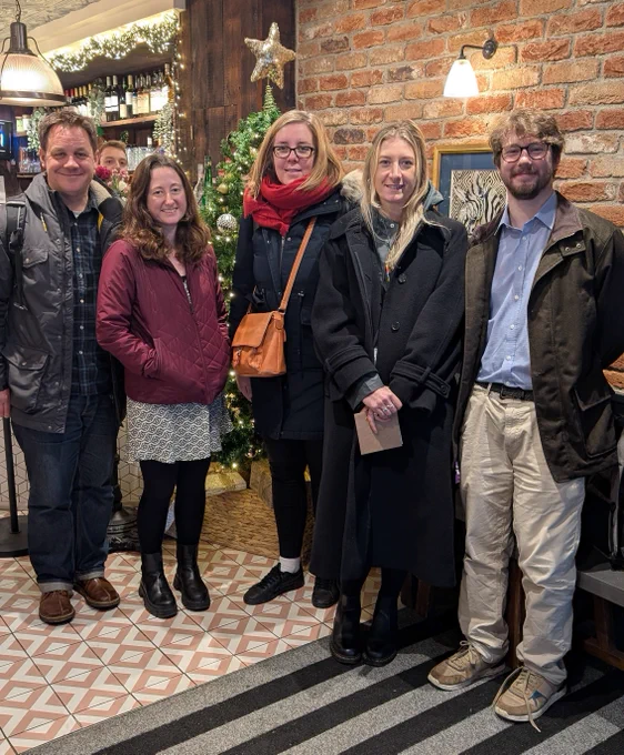 Five members of the pro2 team stand in front of a Christmas tree in a restaurant, smiling and facing the camera.