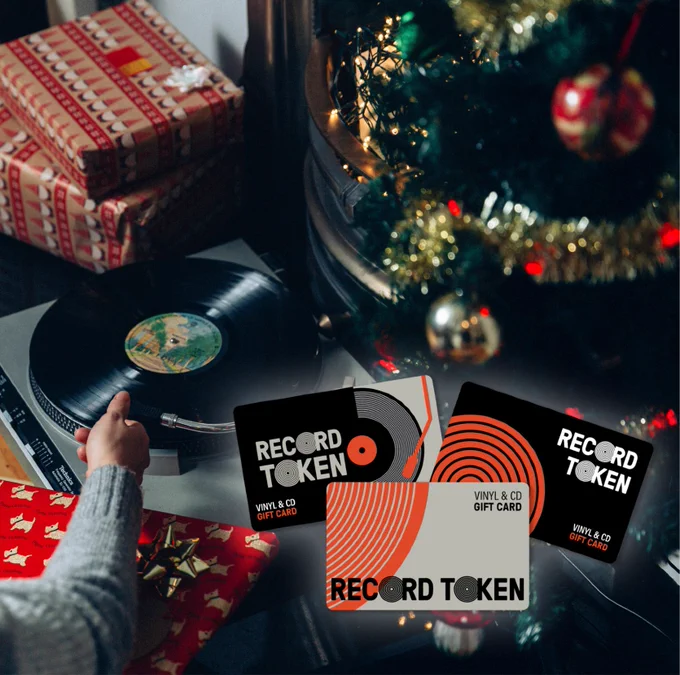 A record player is positioned underneath a Christmas tree surrounded by wrapped presents and decorations. Three Record Tokens are featured in the corner of the image.