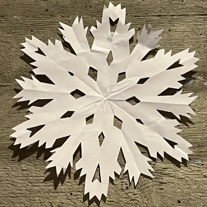 A snowflake made from folded and cut white paper and stuck to a concrete wall