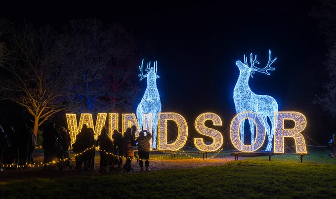 Photo of guests at a light trail in Windsor Great Park. They are standing in front of the word 'Windsor' in golden lights, with two huge sculptures of deer lit in white. 