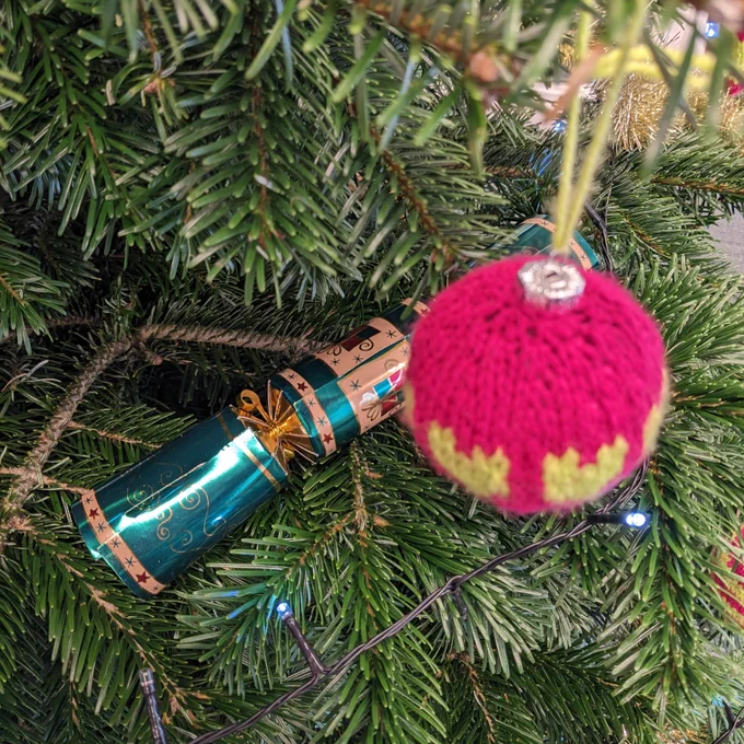 A knitted bauble and a cracker hang from a Christmas tree