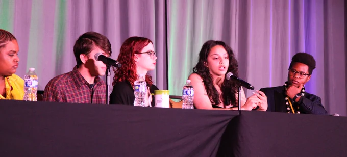 Youth panelists are seated at a table in a discussion during the National Grantee Training plenary, with microphones in front of them.