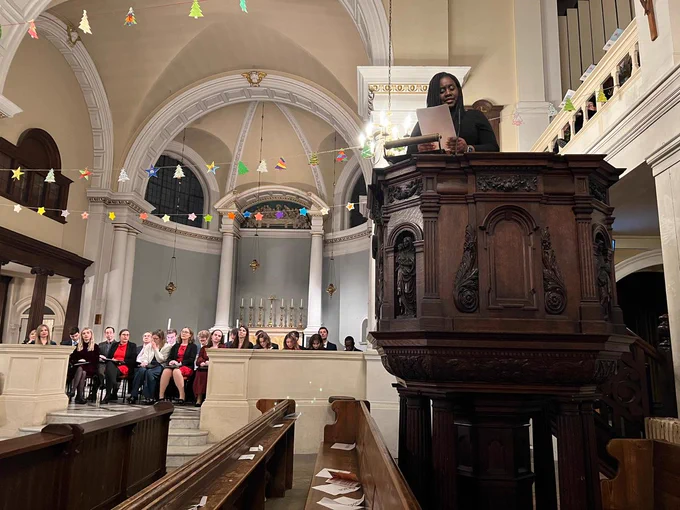 Marsha stood at a podium in a Church giving a reading at the Carol service