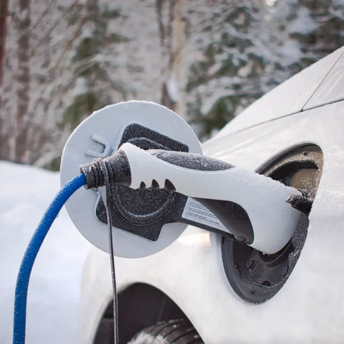 EV charger plugged into a white car outside in the snow.