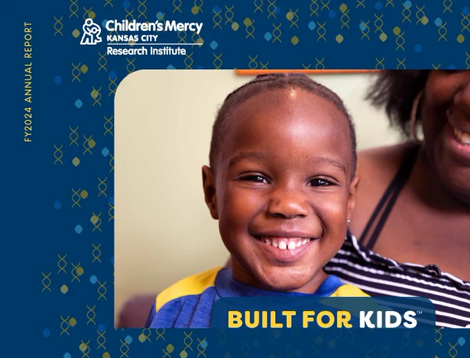 The cover of the FY2024 Annual Report for the Children's Mercy Research Institute. It has a darker blue background and over that are small images that look like tiny drops in the colors of blues and yellows along with small helix shapes. A photo of a young boy sitting on his mother's lap smiling directly into the camera is the main part of the cover. It also says "Built for Kids" along the bottom.