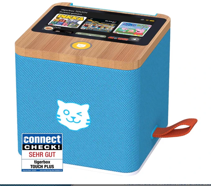 Das Bild zeigt eine tigerbox TOUCH, ein würfelförmiges Audiogerät für Kinder. Es hat folgende Eigenschaften:
Hellblaues Gehäuse aus texturiertem Material mit einer Holzoptik-Oberseite
Touchscreen-Display auf der Oberseite, das aktuell verschiedene Kinderinhalte wie "Die Olchis" und "Peppa Pig" anzeigt
Weißes Katzen-Logo auf der Vorderseite
Braune Lederschlaufe an der Seite
Ein "Connect CHECK!" Testsiegel mit der Bewertung "SEHR GUT" für die tigerbox TOUCH PLUS vom November 2023