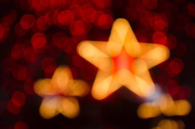 Image shows shining gold Christmas star decorations on a red tinsel background