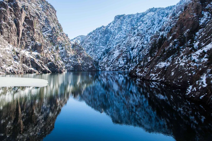 A calm reservoir surrounded by snow-covered cliffs and rugged mountains. 
