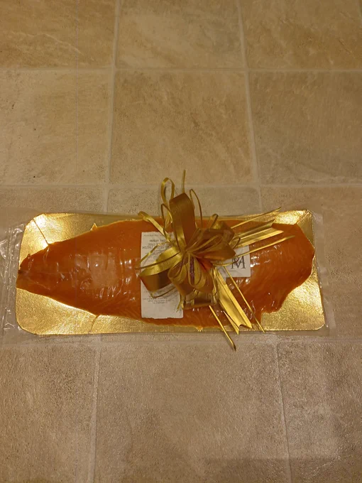 A large pack of smoked salmon, on cardboard, vacuum packed with a big ribbon and bow on top