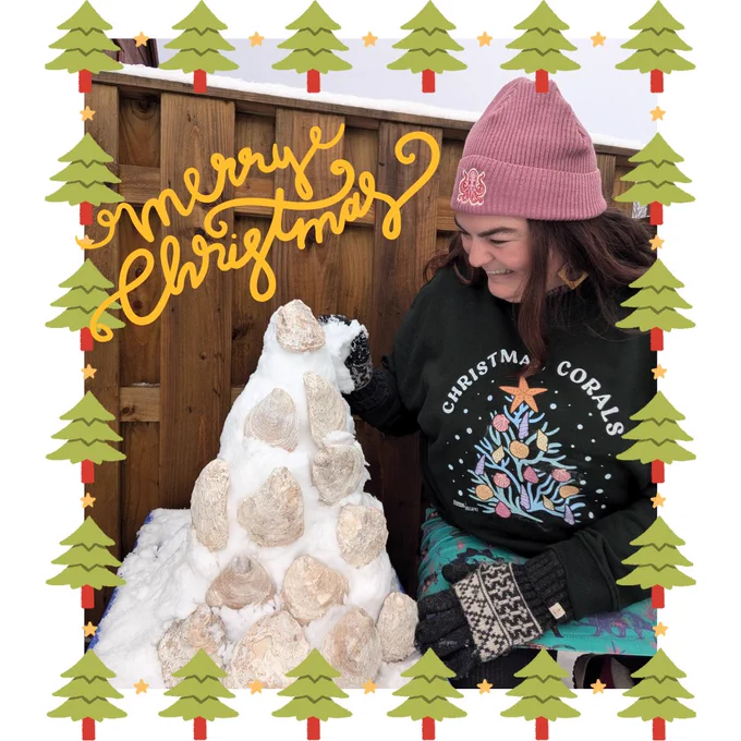 Catherine wearing a christmas jumper with a christmas tree of corals, a pink beanie next to a small snow christmas tree with oyster shells