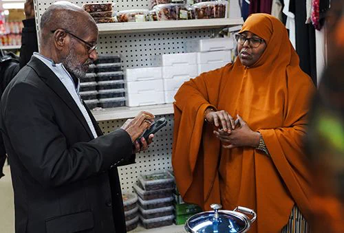 Photo shows Idris Mohamed of African Economic Development Solutions meeting with a client at an African grocery store. The female client wears an orange jilbab.