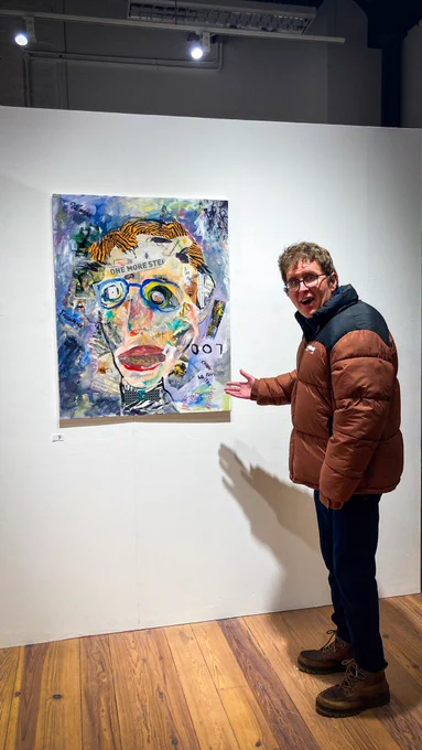 Man standing beside a painting of a face.