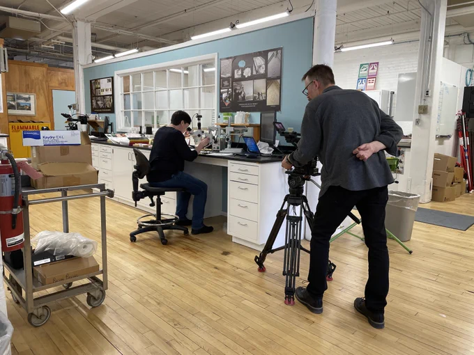 A videographer films a person seated at a conservation work station. 
