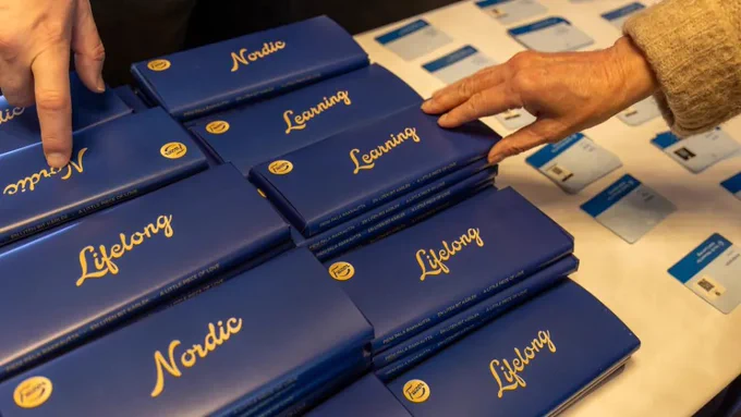 Blå förpackningar som det står antingen "Lifelong" eller "Nordic" på. I hörnet finns logotypen för Fazer. Händer sträcks fram för att ta förpackningar. Allt tyder på att det är choklad i dem.
