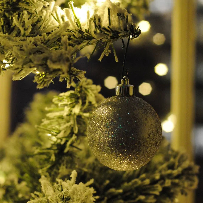 A glittery Christmas bauble hanging from a snow-dusted Christmas tree.