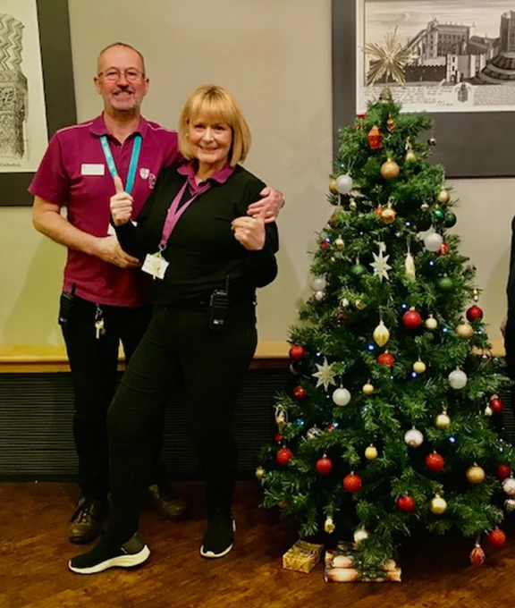 Two of our visitor service staff posing beside the Christmas Tree at Palace Green Library reception. 