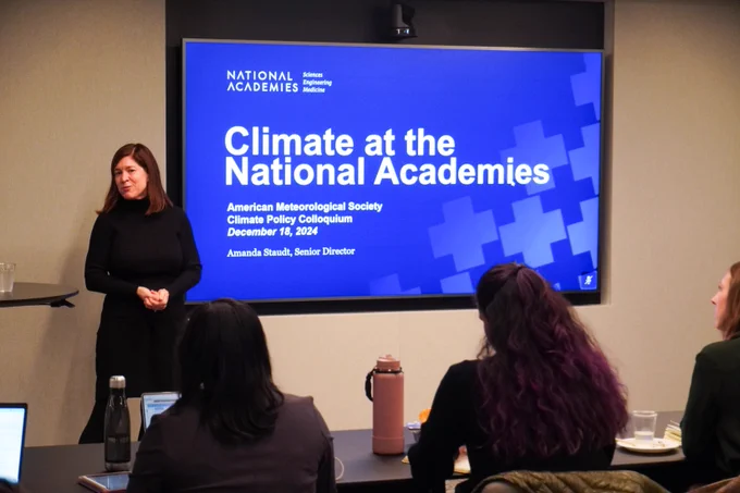 A woman presents to an audience a blue screen about Climate at the National Academies at the AMS Climate Policy Colloquium.