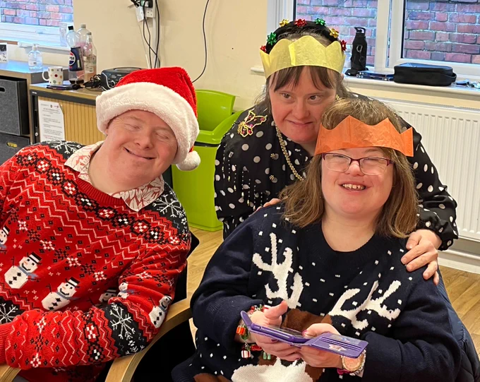A man and two women who are wearing festive hats and festive jumpers are smiling at the camera.