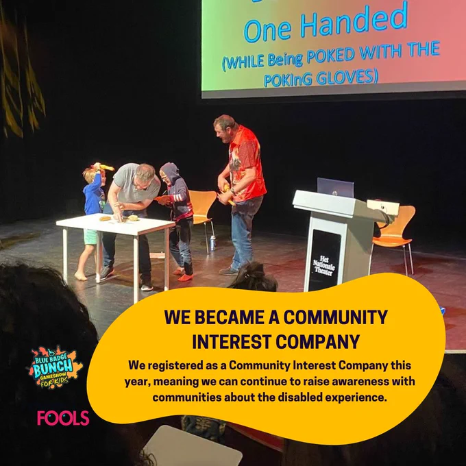 Two children and two performers on stage during a Blue Badge Bunch show, with a large presentation screen behind them, with a caption about registering as a a Community Interest Company this year.