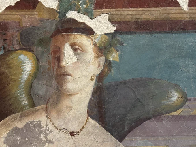 The portrait of a winged female genius. She wears a gold necklace which has a red stone pendant, and gold earrings.