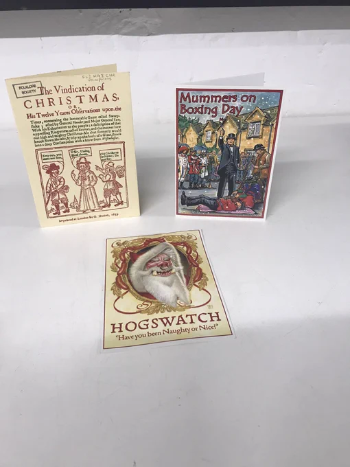 Three Christmas cards. One is a reproduction of the 17th century pamphlet “A Vindication of Christmas”, an illustrated card of a doctor reviving a hero with the title “Mummers on Boxing Day”, and a postcard with a portrait of Terry Pratchett’s character the Hogfather which reads “Hogswatch, have you been naughty or nice!”