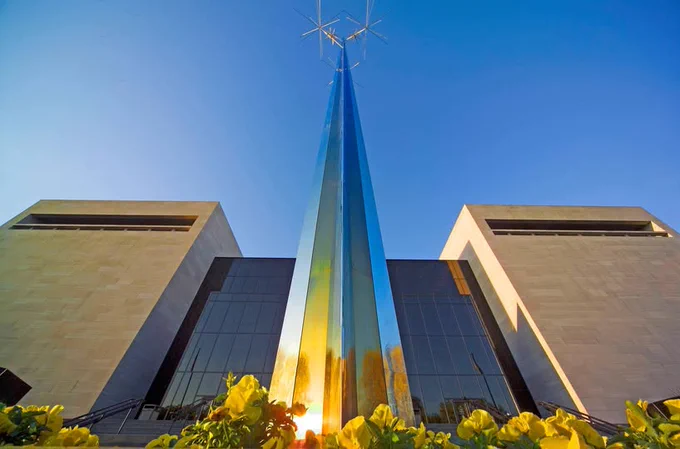 Sunset view of the National Air and Space Museum, featuring a tall, stainless-steel sculpture with a pointed tip, that almost looks like it's penetrating a triple star-like cluster near its apex.