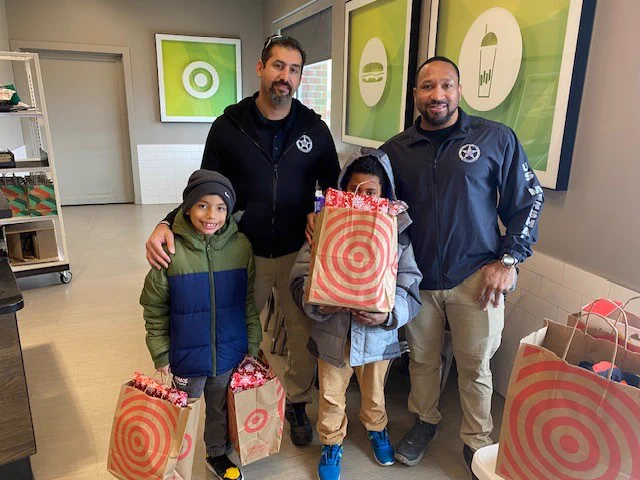 Two Deputy U.S. Marshals pose with two children and the gifts purchased for the holidays. 