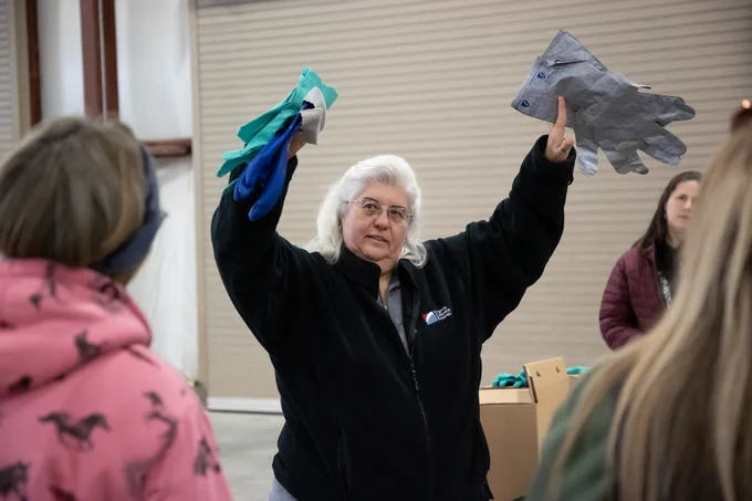 A person in a Virginia Cooperative Extension jacket hands out safety gloves