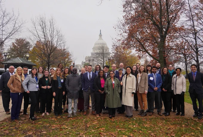 A group of people posing for a photo in front of the United States Capitol building on an overcast day.