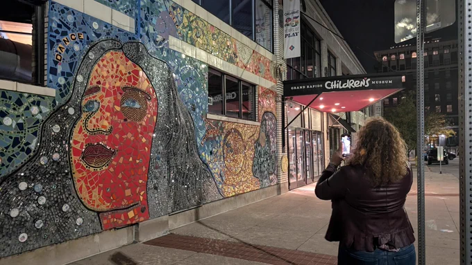 African American woman taking photo of colorful mural made of tiles