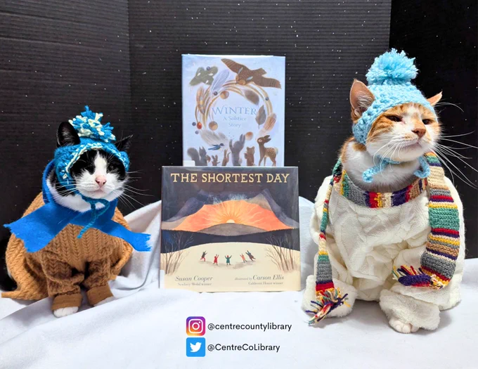 A photo of Horatio the Cat and Jojo the Pirate Cat dressed in hats, scarves, sweaters sitting next to the books "The Shortest Day" and "Winter: A Solstice Story." 