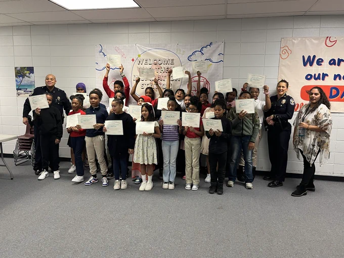 A class of students, adults, and two police officers pose for a picture.