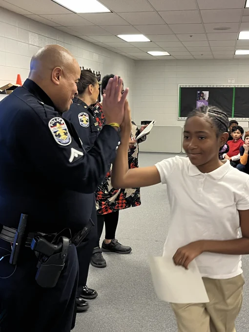 A student high-fives a police officer while holding a certificate.