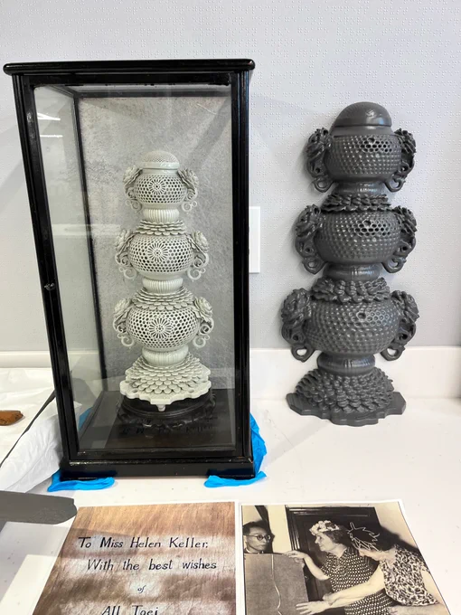 A display featuring two intricate incense burners, the orginial behind glass and a slightly larger replica beside it. In front of the incense burners, a note addressed to "Miss Helen Keller" lays beside a historical photograph featuring Helen Keller.