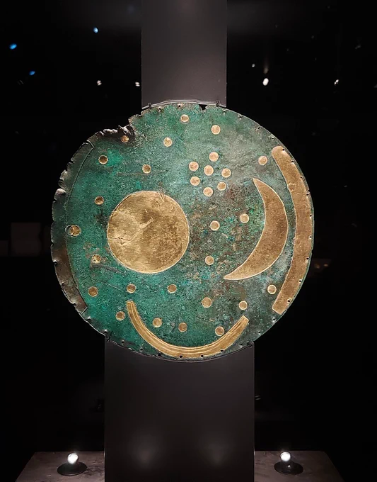 A photo of a museum display with the Nebra sky disk. The green coloured bronze disk features a gold sun, moon and star decoration.