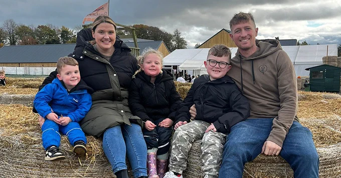 A family of five sitting on hay bales at a farm, smiling contentedly.
