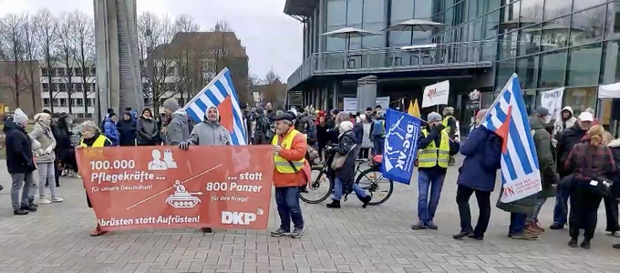 Eine Gruppe von Menschen vor der Osnabrückhalle. Im Vordergrund zwei Männer mit Fahnen der VVN-BdA, ein Mann mit Fahne der DFG-VK, zwei Männer und eine Frau halten ein Banner der DKP