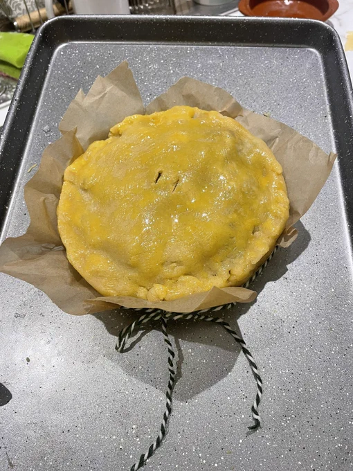 A large pie with a shiny top, tied in paper with a bow in stripy string, ready to go in the oven